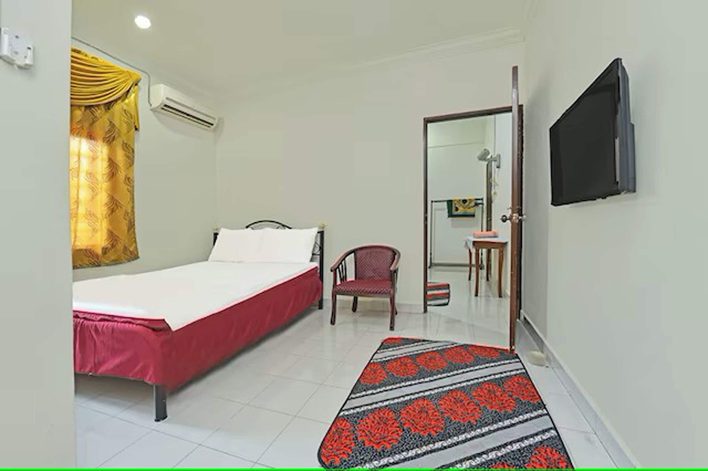 Una habitación con una cama, una silla, una mesita y un televisor montado en la pared.