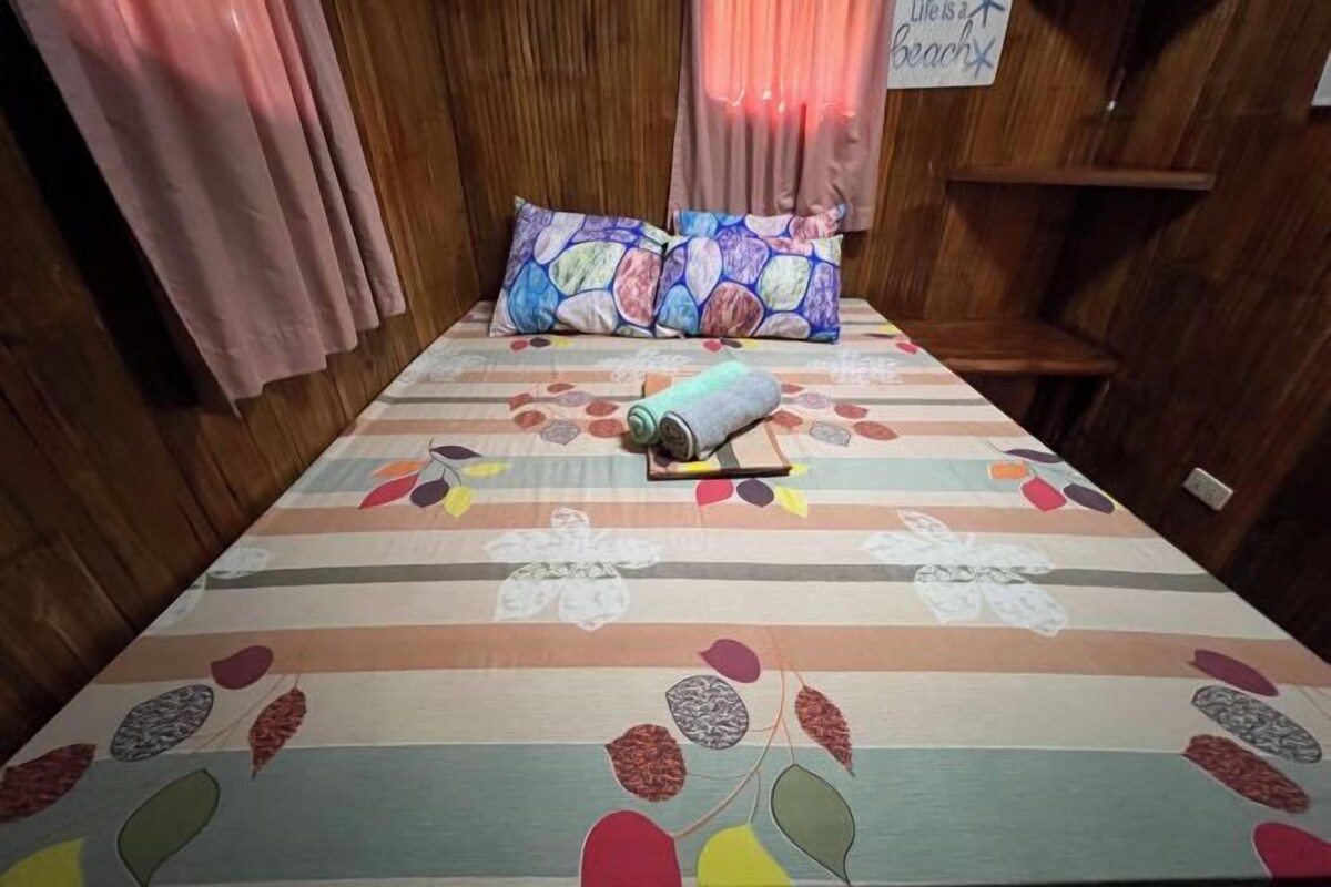 A bed with a colorful striped bedspread and two patterned pillows, a rolled-up towel, and a sign on the wall that reads "Life is a beach."