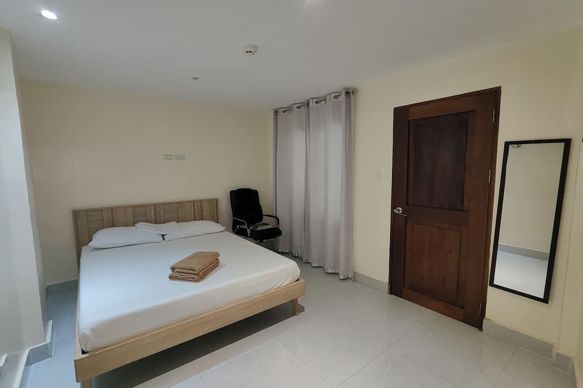 Un dormitorio con cama, una silla, una puerta y un espejo.