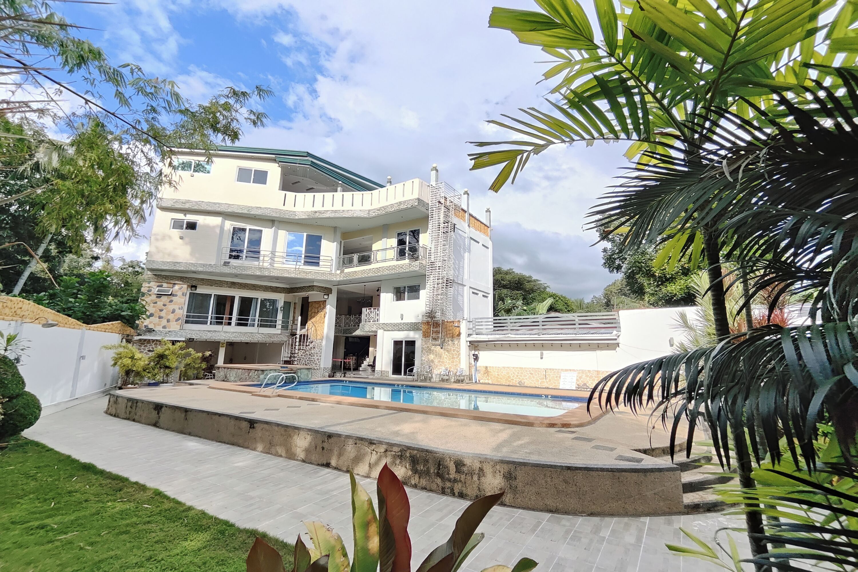 A multi-story house with a swimming pool, surrounded by greenery and a white fence.