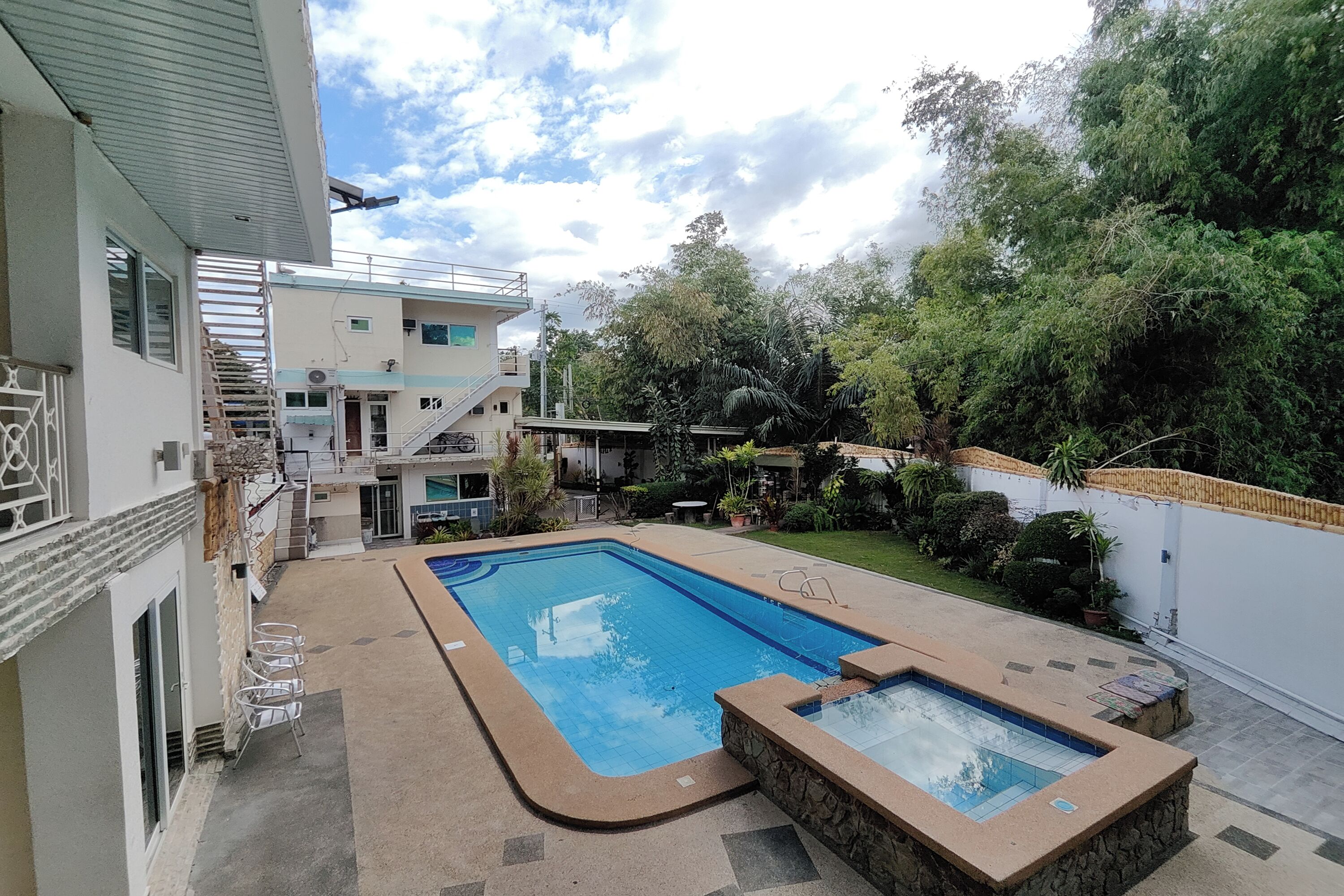 A swimming pool with a stone surround, a covered seating area, and a staircase leading to a multi-level building.