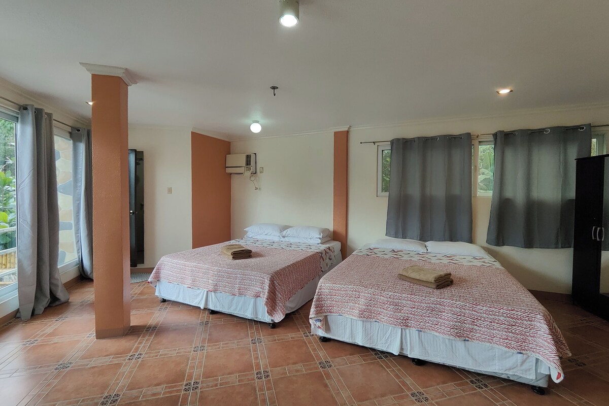 A hotel room with two beds, a window with curtains, an air conditioning unit, and a tiled floor.