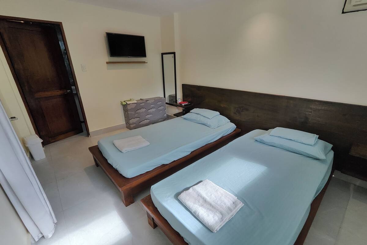 Habitación de hotel con dos camas individuales, un televisor montado en la pared y un espejo sobre la cama.