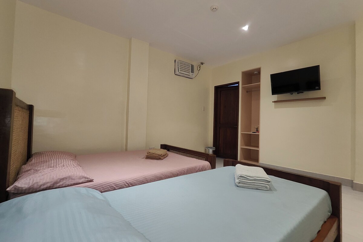A room with two single beds, a TV mounted on the wall, and a wooden wardrobe.