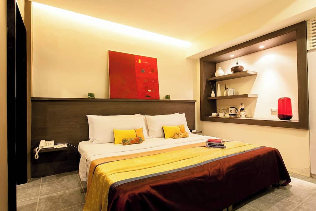 A hotel room with a bed, bedside table, and a shelf with decorative items.