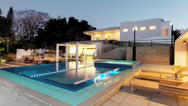Un área de piscina moderna con una piscina cristalina, una zona de estar techada y una escalera que lleva a un edificio.