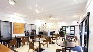 Un comedor moderno con varias mesas y sillas, una zona de cocina con estantes y vistas al exterior.