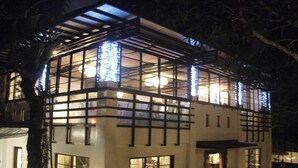 Un edificio moderno con ventanas amplias y una sección superior cubierta.