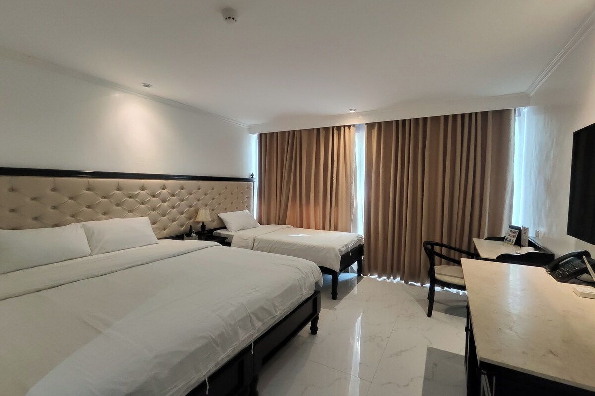 A hotel room with two beds, a desk, a chair, and a TV.