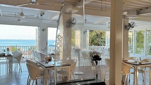 A spacious indoor area with a view of the sea, featuring white furniture, a black piano, and ceiling fans. - The Mark Resort (Lapu-Lapu)