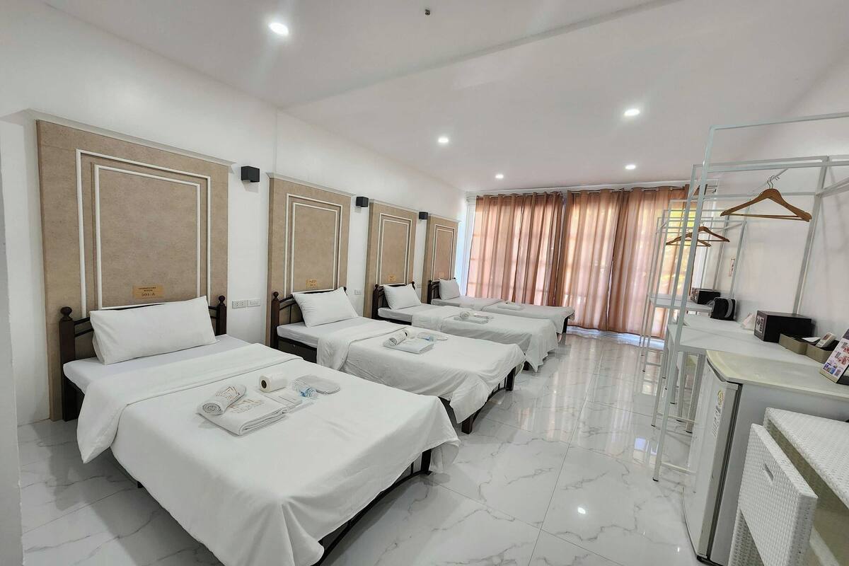 A hotel room with four single beds, each with a white bedspread and a small tray with towels.