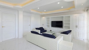 A spacious living room with a large white sofa set, a flat-screen TV, and built-in shelving. - The Mark Resort (Lapu-Lapu)