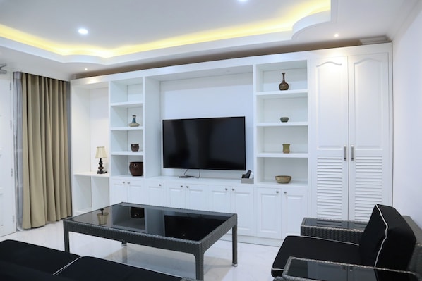 A modern living room with a flat-screen TV, white cabinetry, and a glass coffee table.
