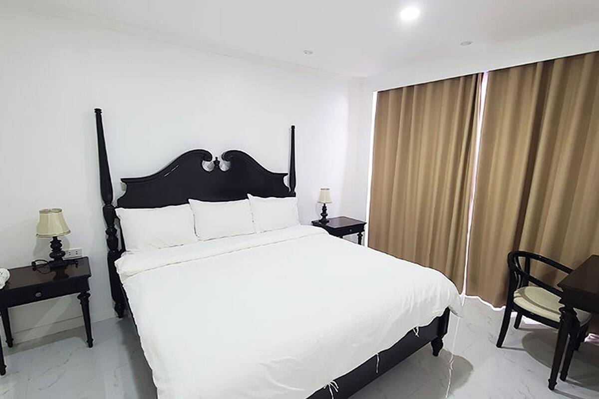 A hotel room with a large bed, two bedside tables, a chair, and a window with curtains.