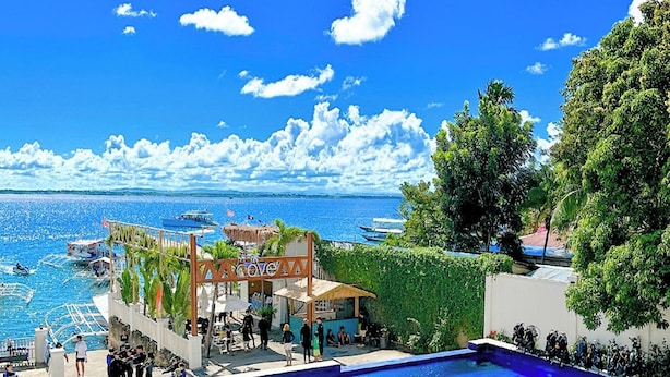 A swimming pool with a view of the sea, surrounded by umbrellas and a shaded area. - The Mark Resort (Lapu-Lapu)