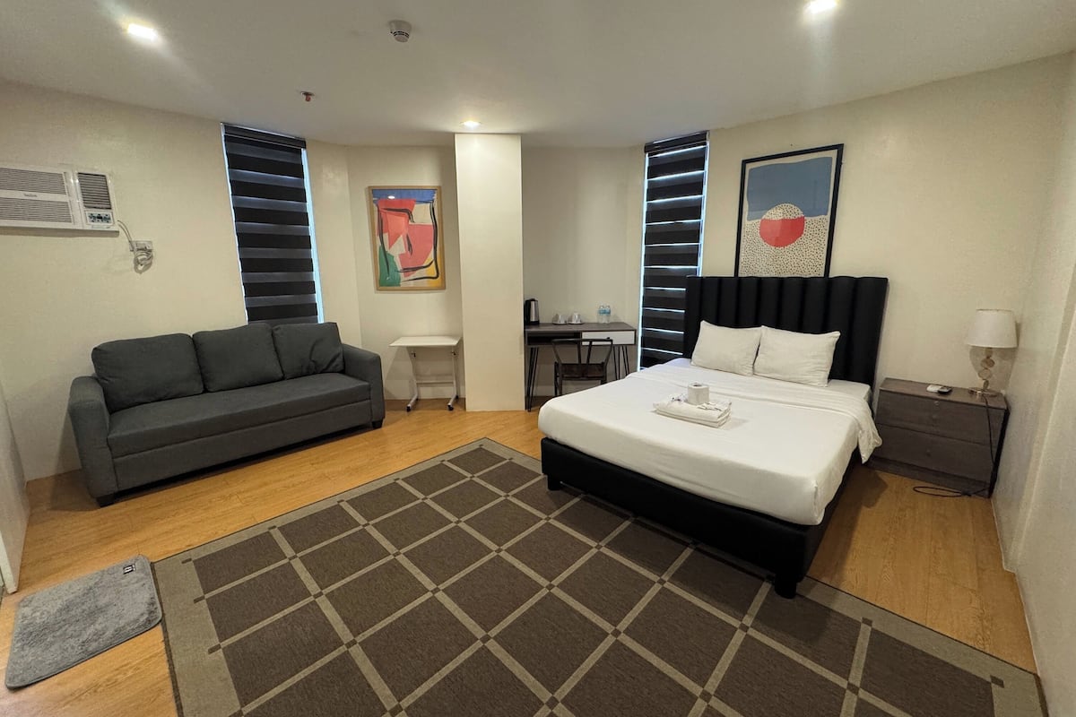 A modern hotel room with a bed, a sofa, a desk, and a chair.