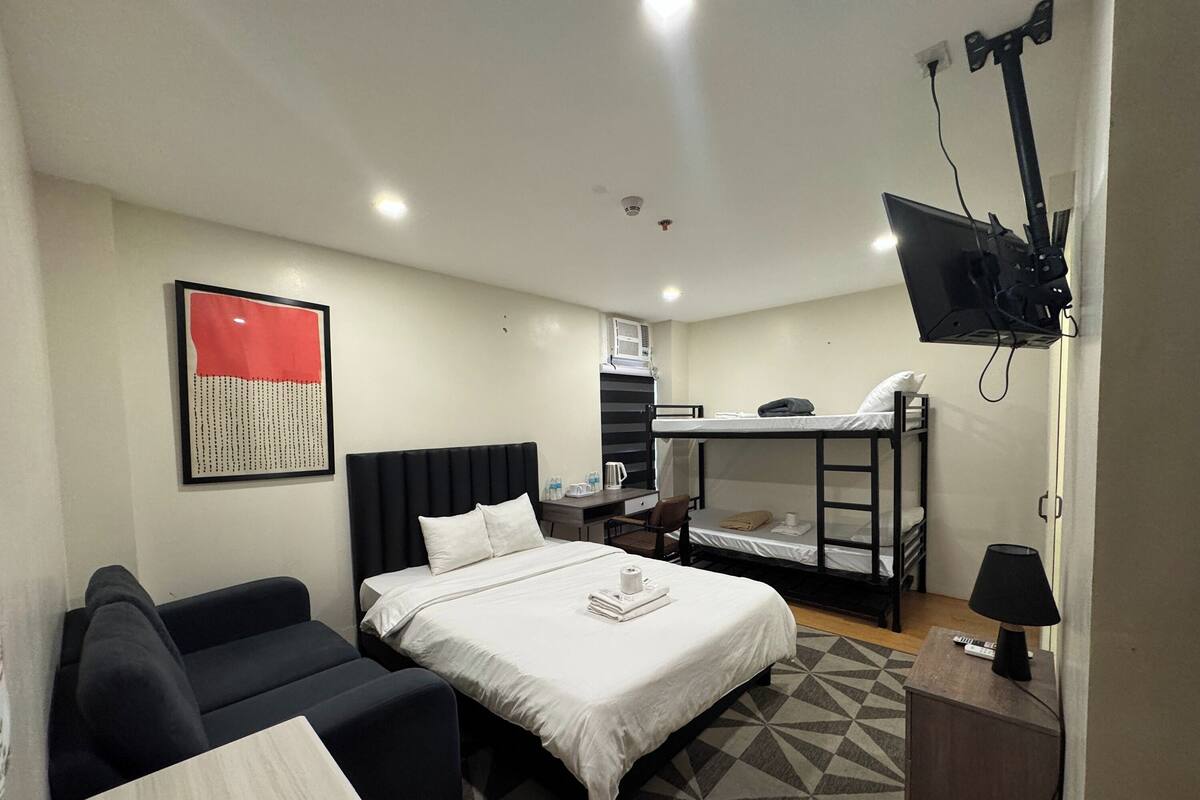 A hotel room with a bed, a couch, a desk, a TV mounted on the wall, and a bunk bed.
