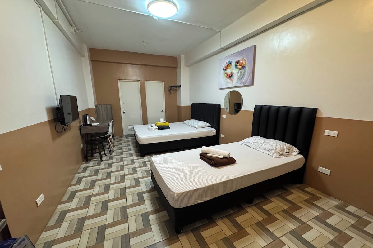A hotel room with two beds, a desk with a chair, a TV, and a painting on the wall.