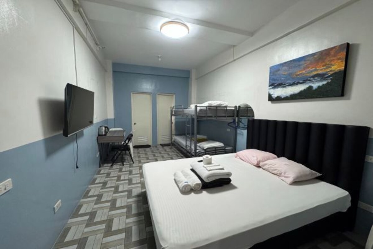 A hotel room with bunk beds, a flat-screen TV, a painting, and a patterned floor.