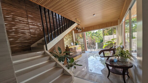 A modern interior with a wooden staircase, a reception desk, and a glass door leading outside. - Manuela Suites Puerto Princesa near Airport (Puerto Princesa)