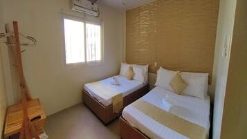 A room with two beds, a window, and an air conditioning unit.