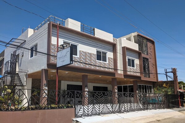 A two-story residential building with a covered parking area, a metal fence, and a clear blue sky.