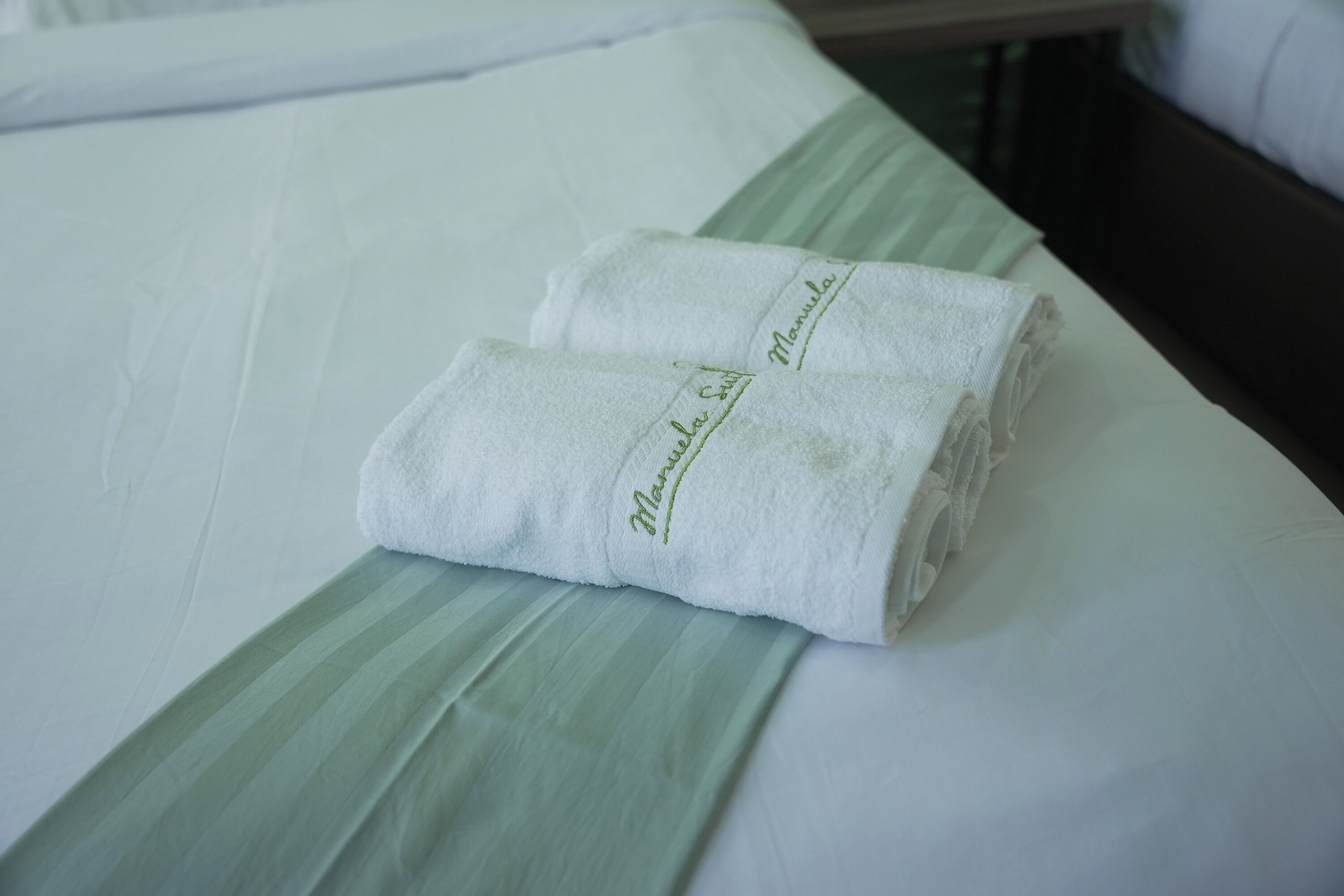Un lit bien fait, avec du linge de lit blanc et deux serviettes pliées, ornées d’un motif brodé.
