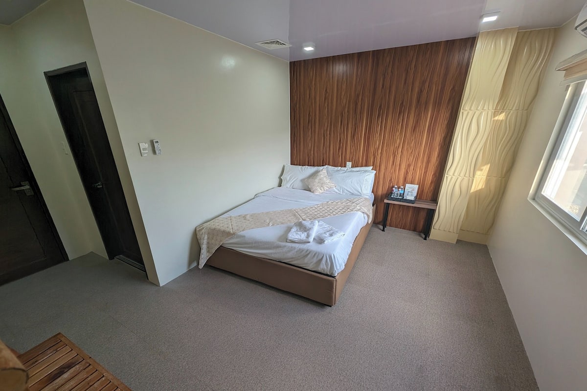 A bedroom with a bed, a nightstand, a wooden door, and a window with curtains.