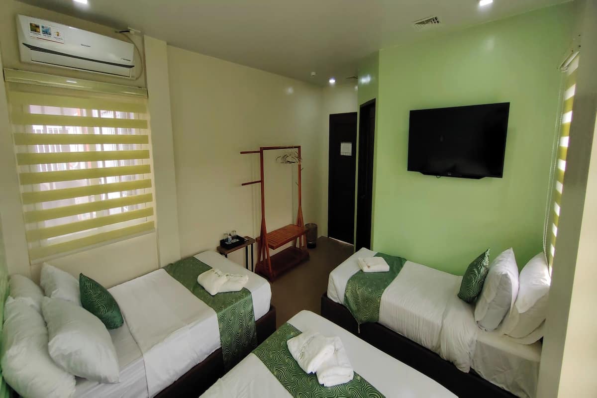 A hotel room with two beds, a TV, an air conditioner, and a window with blinds.