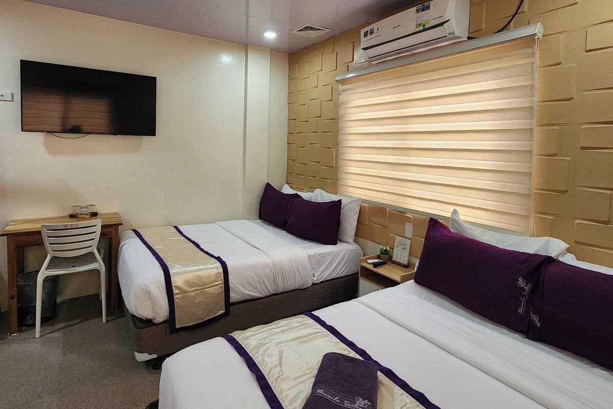 A hotel room with two beds, a desk, a chair, an air conditioning unit, and a television.