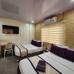 A hotel room with two beds, a desk, a chair, an air conditioning unit, and a television.