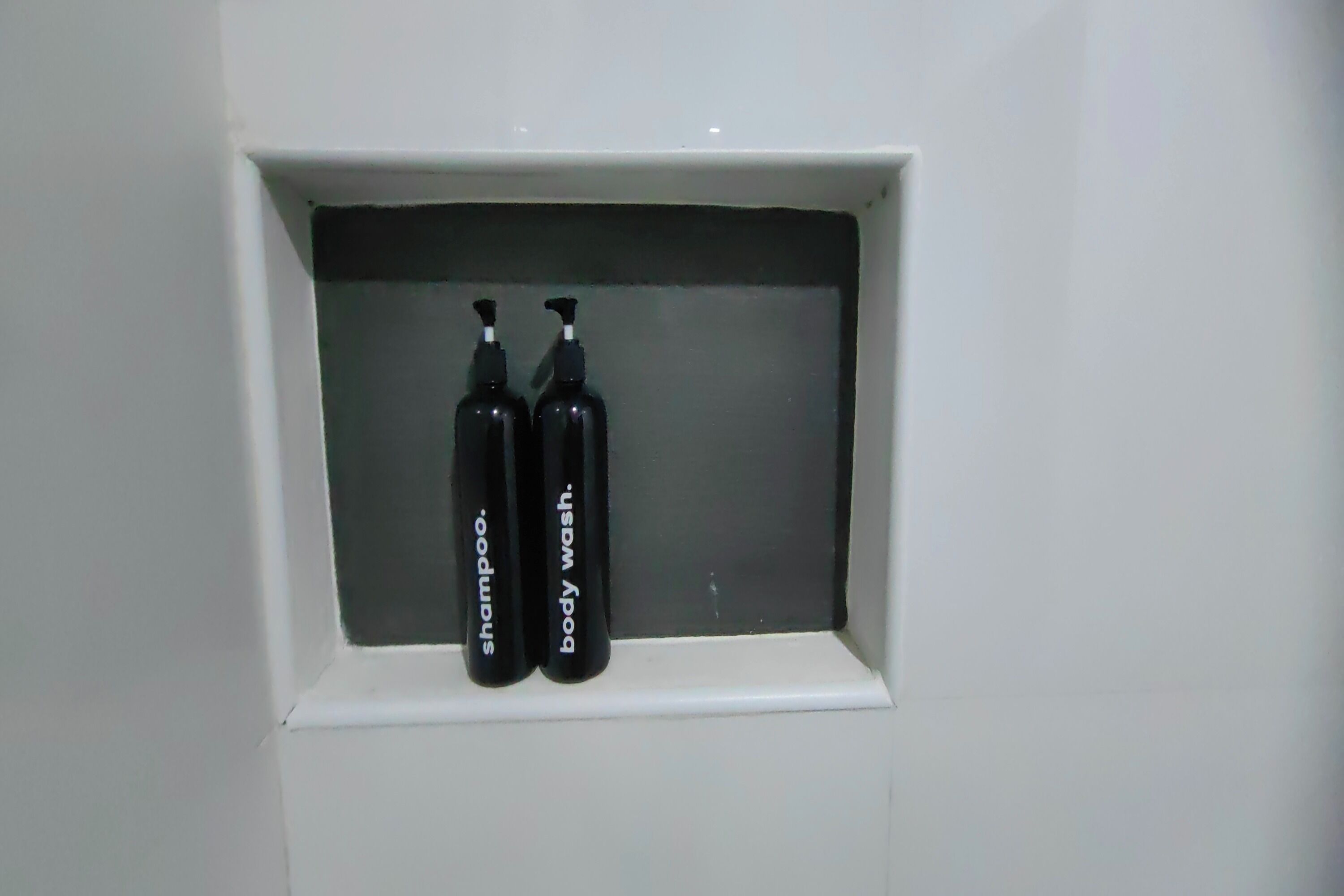 A white shelf with two black bottles labeled "shampoo" and "body wash."