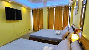 A hotel room with two beds, a flat-screen TV, curtains, a bedside table with a lamp, and a mirror. - Inn Ka Kay Mame near SM City Puerto Princesa (Puerto Princesa)