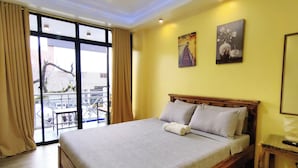 A hotel room with a large bed, a wooden headboard, a small bedside table, and a view of the outside balcony. - Inn Ka Kay Mame near SM City Puerto Princesa (Puerto Princesa)
