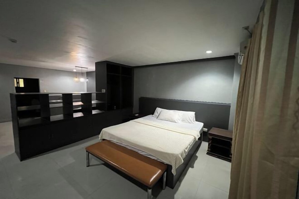 Ein modernes Schlafzimmer mit einem großen Bett, einer Bank, einem Fernseher und einem Kleiderschrank.