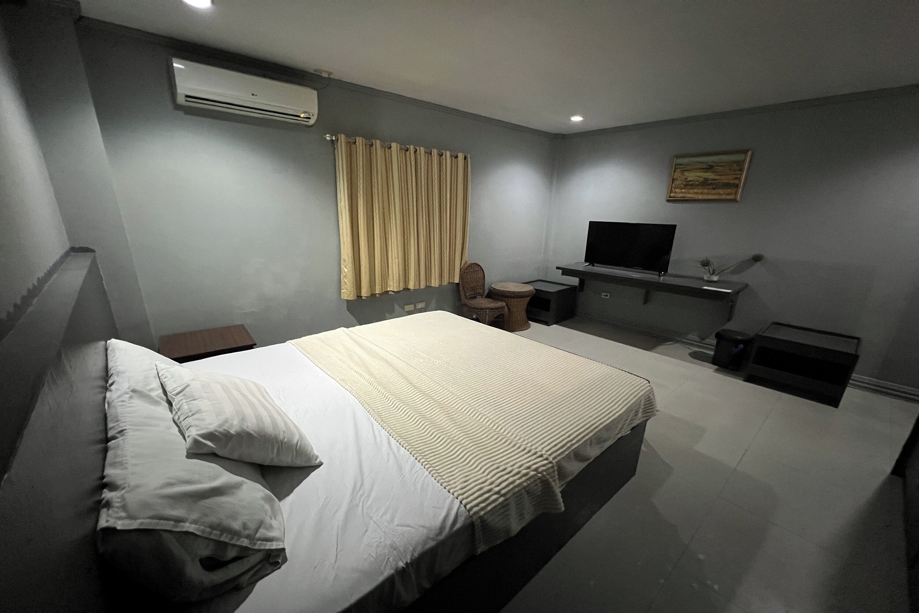 A bedroom with a bed, a desk, a chair, a television, and a painting on the wall.