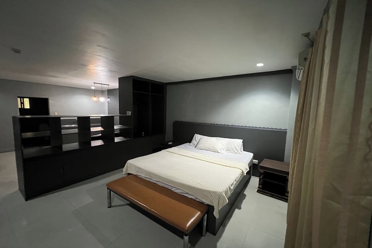 Une chambre moderne avec un grand lit, un banc, une table de chevet et une armoire.
