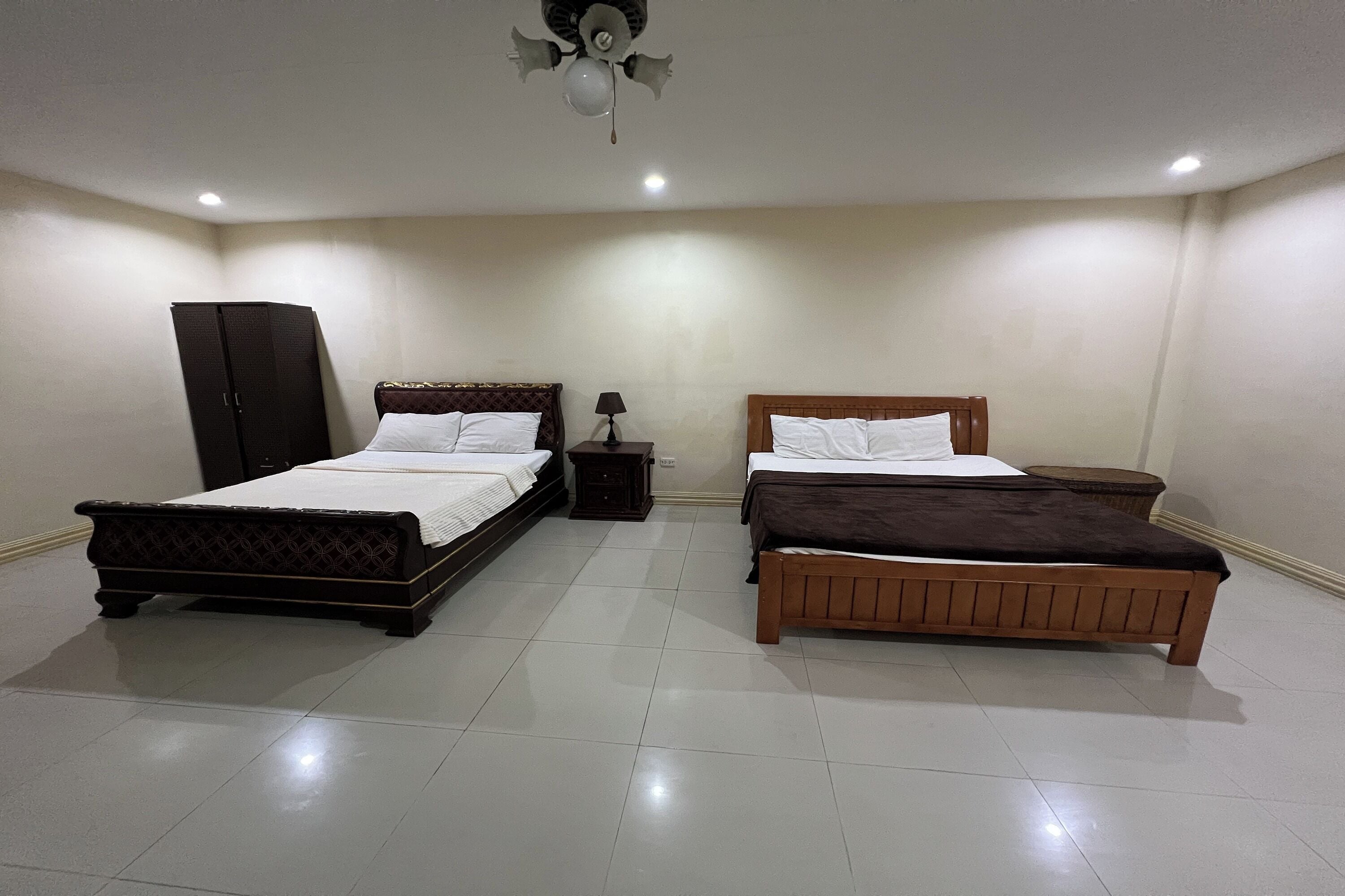 A bedroom with two beds, a wardrobe, a nightstand, and a ceiling fan.
