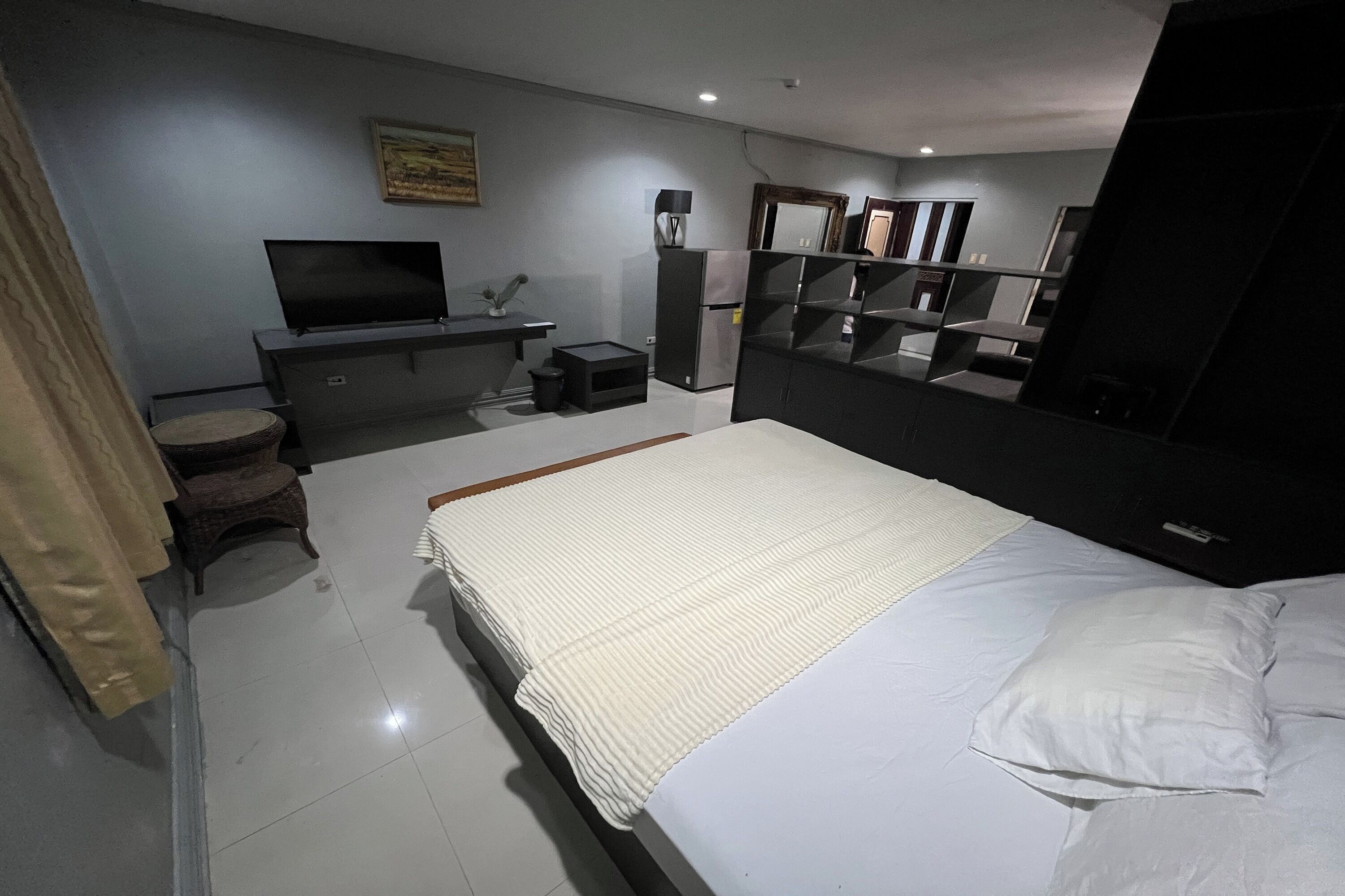 A bedroom with a bed, a TV, a dresser, a mirror, and a small seating area.