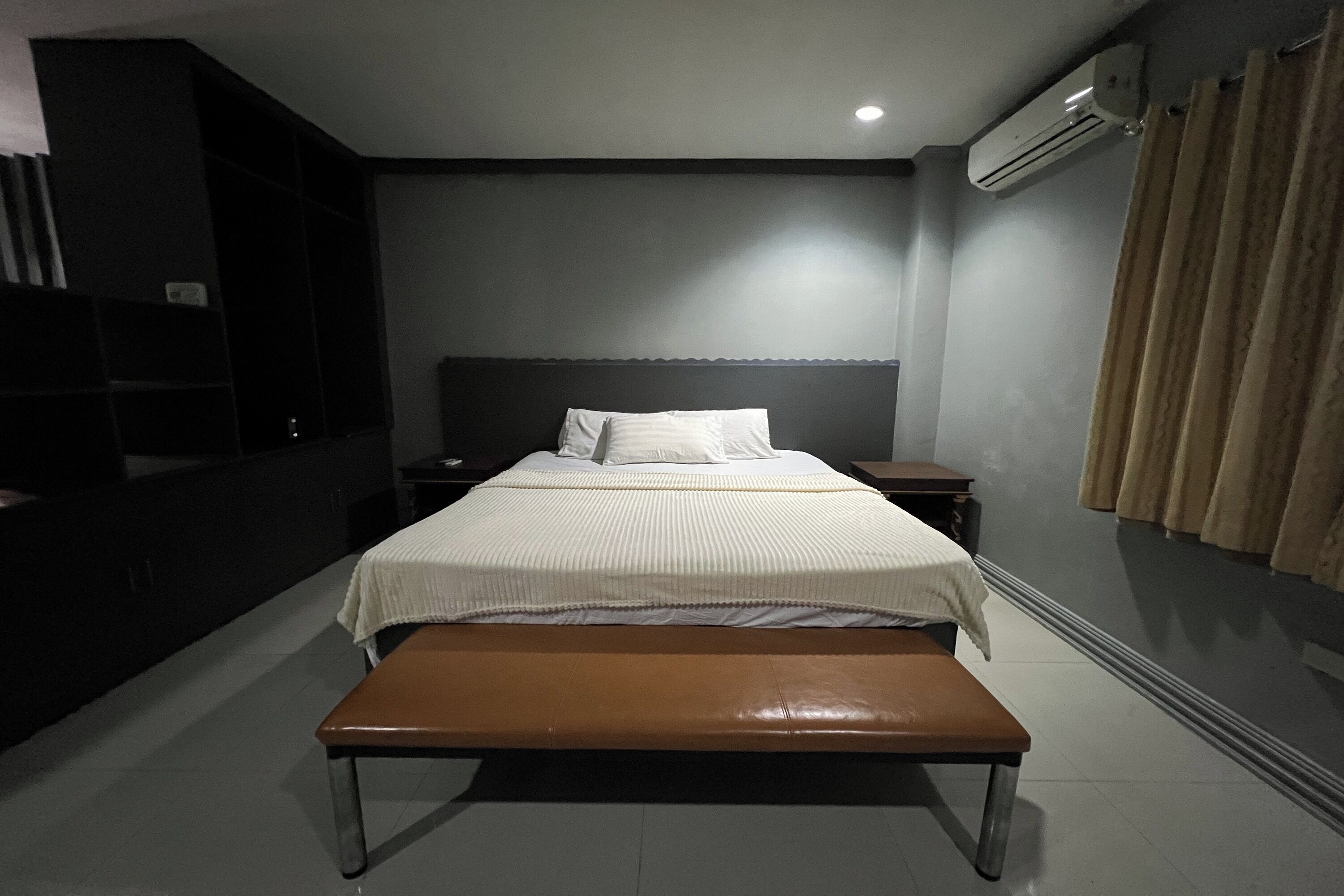 Una habitación de hotel moderna con una cama grande, un banco, una mesita de noche y un televisor. También se aprecia un equipo de aire acondicionado.