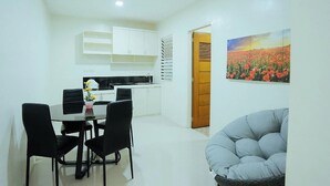 A modern kitchen with white cabinets, a dining table with black chairs, and a painting of a field of flowers on the wall. - Ljenj Apartelle (Mabalacat City)