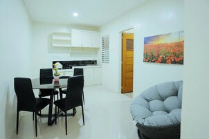 A modern kitchen with white cabinets, a dining table with black chairs, and a painting of a field of flowers on the wall.
