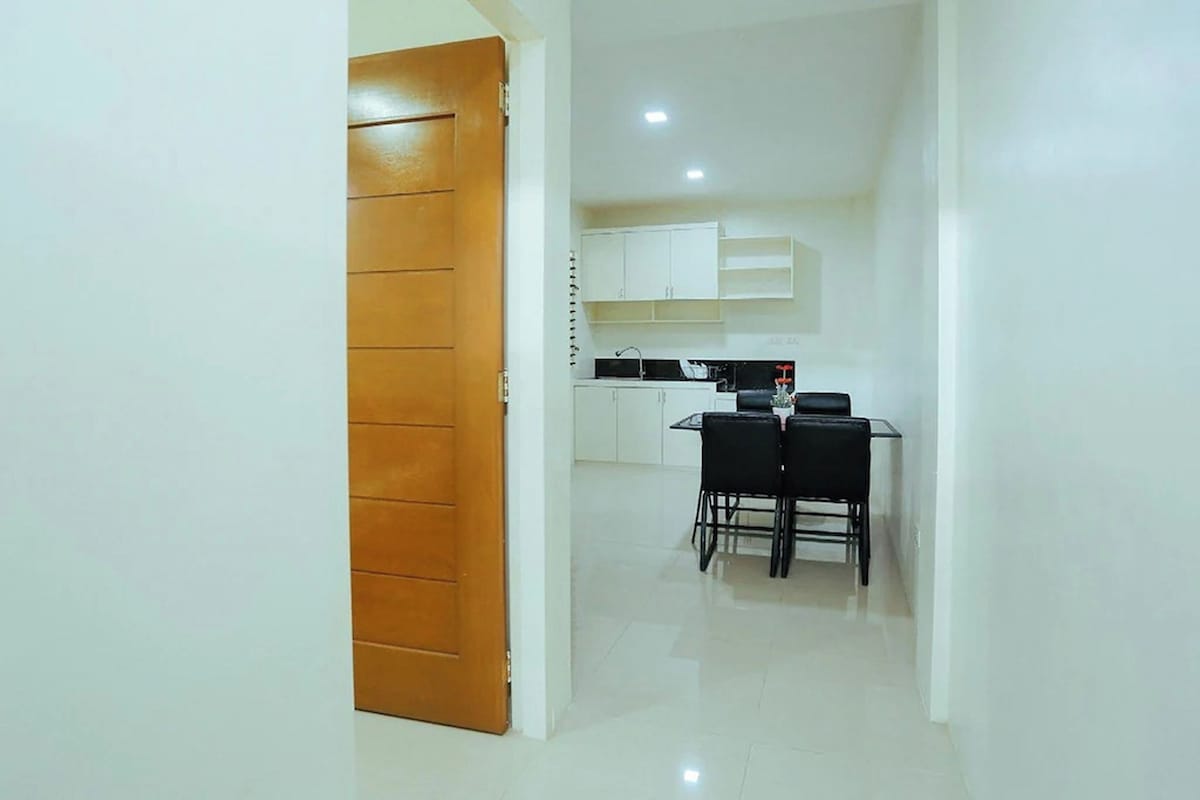 A hallway leading to a kitchen with white cabinets and a dining table with chairs.
