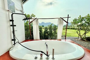 A bathroom with a large bathtub, a shower system, and a view of a green landscape with mountains. - Idin Klin Pha Man (Phupa Man)