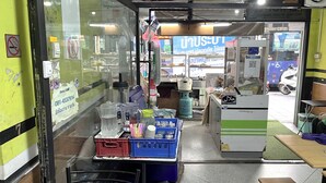 A small, cluttered room with a table, chairs, and various items on display. - Ali Hostel (Bangkok)