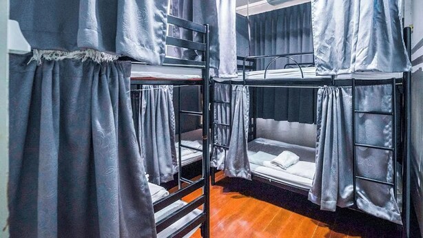 A dormitory room with bunk beds, grey curtains, and a wooden floor. - Ali Hostel (Bangkok)