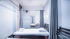 A single-bed room with a metal frame, a small table with a chair, and a window with curtains. - Ali Hostel (Bangkok)