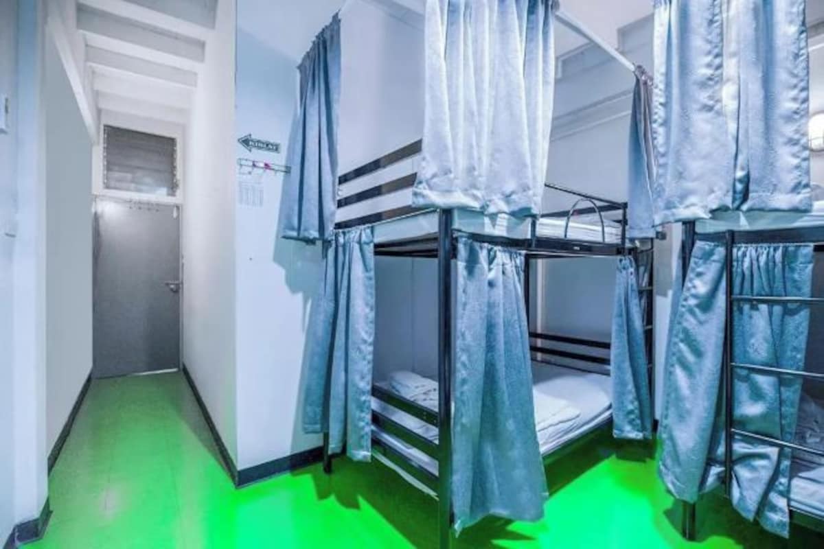A dormitory room with bunk beds, a green floor, and a door leading to another room.