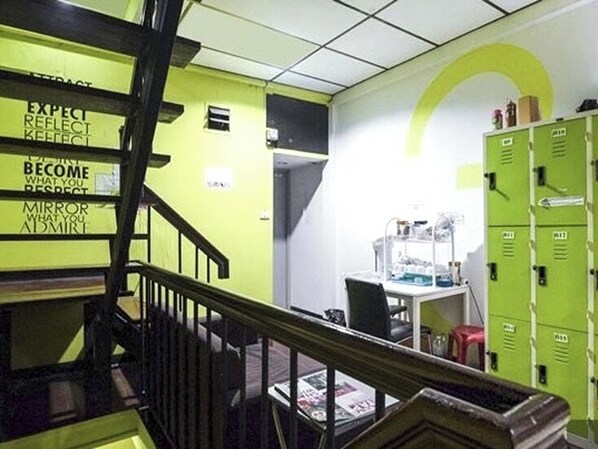 A staircase with a handrail leading to a room with green lockers and a desk with a computer. - Ali Hostel (Bangkok)