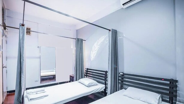 A hotel room with two beds, a large mirror, and a window with curtains. - Ali Hostel (Bangkok)